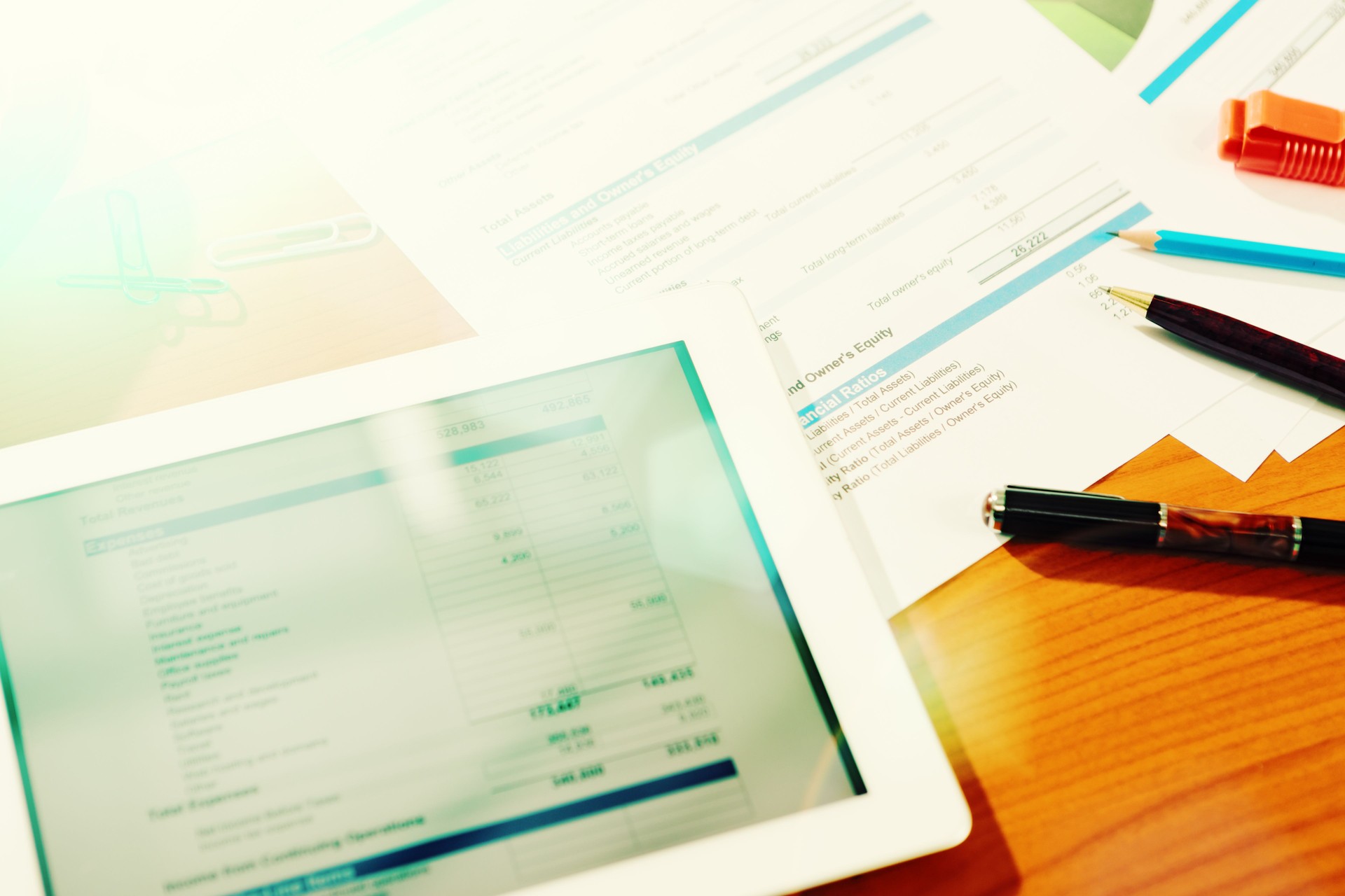 Figures and financial statements on tablet with  printouts on desk